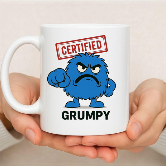 A women holding a white ceramic 11oz Mug. a bright blue grumpy furry cartoon character with a grumpy expression. a red certified stamp above the characters head  with bold text that says Grumpy at the bottom of the mug.