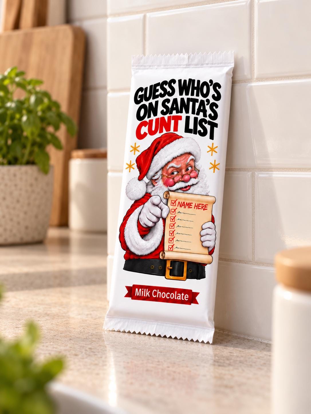 A single milk chocolate bar in a light beige wrapper standing upright on a kitchen countertop. The wrapper features a cartoon Santa holding a scroll with the text 'GUESS WHO'S ON SANTA'S  LIST' and 'Milk Chocolate' at the bottom.